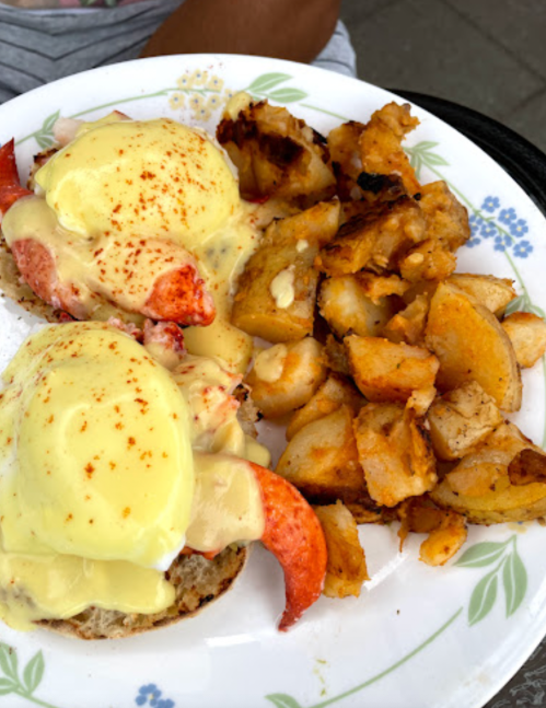 A plate of eggs Benedict with lobster on English muffins, topped with hollandaise sauce, alongside crispy potatoes.