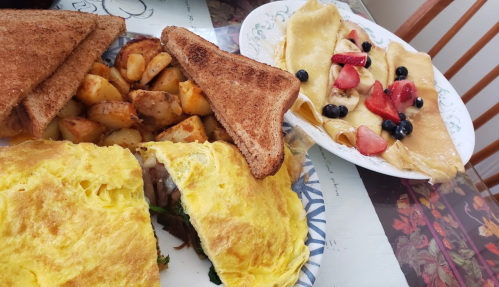 A plate of fluffy omelette with vegetables, crispy potatoes, toast, and a plate of crepes topped with fruit.