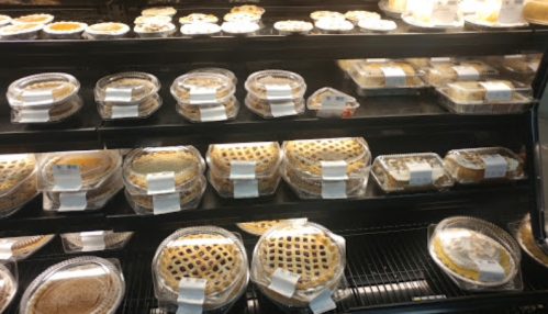 A display case filled with various pies in clear containers, showcasing different crust designs and toppings.