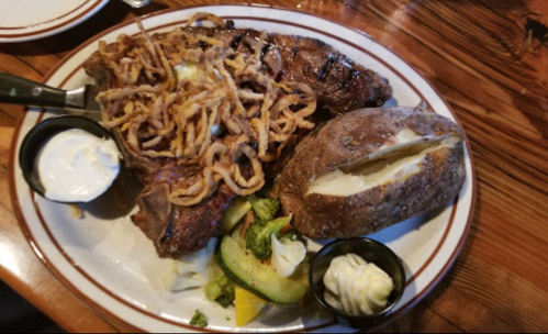A plate featuring a grilled steak topped with crispy onions, a baked potato, and mixed vegetables on a wooden table.