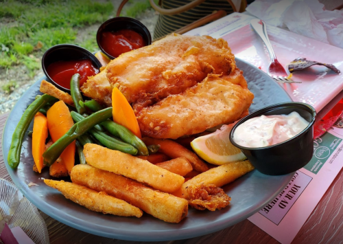 A plate of fried fish fillets with fries, green beans, carrots, and dipping sauces.