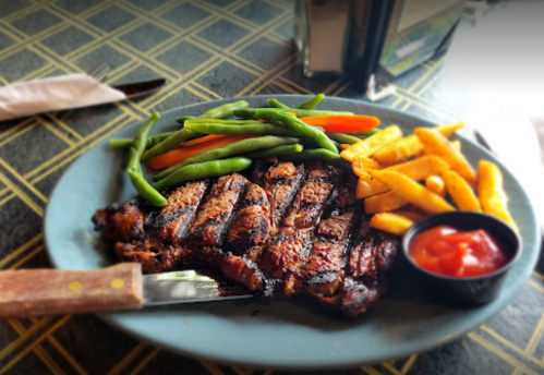 A plate of grilled steak with green beans, carrots, and fries, served with a side of ketchup.