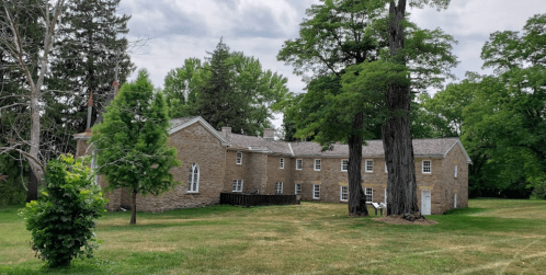 A historic stone building surrounded by lush green trees and grass under a cloudy sky.