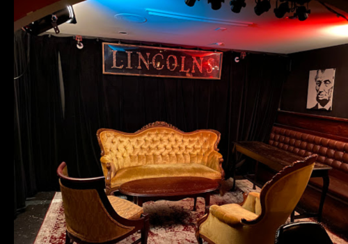 Cozy lounge with vintage furniture, a sign reading "LINCOLN'S," and a portrait of Abraham Lincoln on the wall.