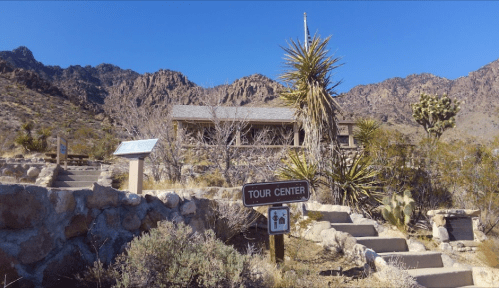 A tour center sign in a desert landscape with mountains in the background and desert vegetation.