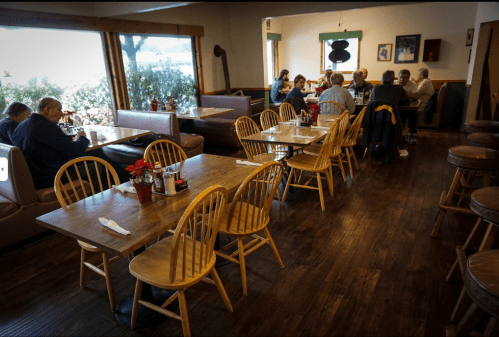 A cozy diner interior with wooden tables and chairs, featuring patrons enjoying meals and chatting.