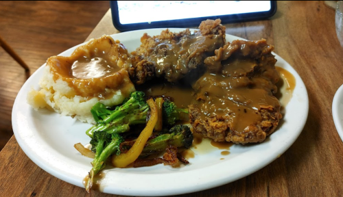 A plate of fried chicken with gravy, mashed potatoes, and sautéed broccoli and bell peppers.