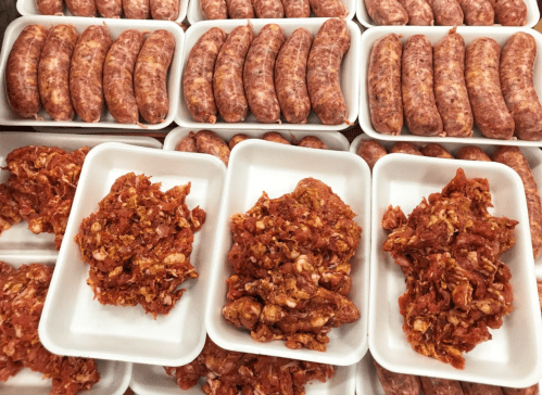 Trays of raw sausages and minced meat arranged neatly on white platters.