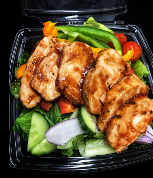Grilled chicken slices on a bed of mixed greens with cucumbers, tomatoes, and bell peppers, drizzled with sauce.
