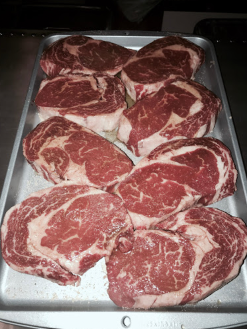 A tray of raw ribeye steaks, marbled with fat, arranged neatly for preparation.