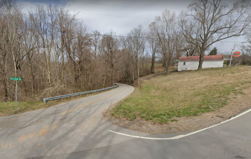 A winding road curves past a grassy area and a small white house with a red roof, surrounded by bare trees.