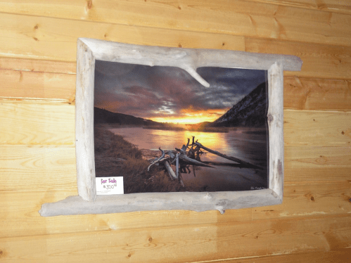 A framed landscape photo of a sunset over a river, with driftwood accents and a price tag for sale.