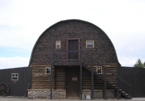 A rustic barn with a rounded roof, wooden siding, and a staircase leading to the entrance, set against a cloudy sky.