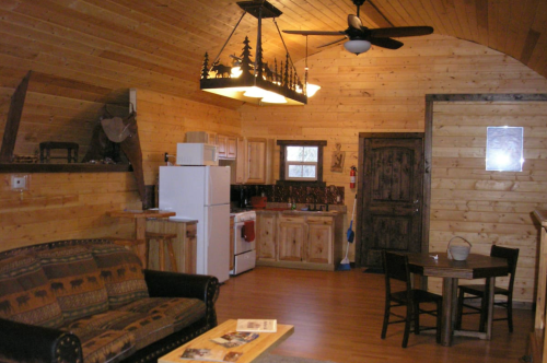 Cozy wooden cabin interior featuring a kitchen, dining area, and living space with rustic decor and a ceiling fan.