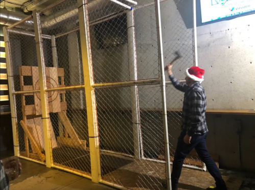 A person in a Santa hat throws an axe at a wooden target inside a fenced area.