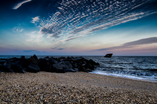 A serene beach scene at sunset, featuring rocky shorelines and a calm sea under a colorful sky.