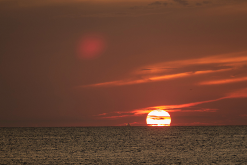 A vibrant sunset over the ocean, with warm orange and red hues reflecting on the water's surface.