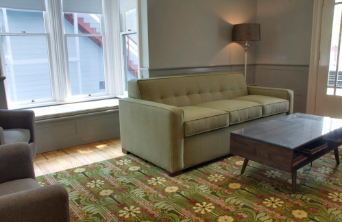 A cozy living room featuring a green sofa, a wooden coffee table, and a patterned rug, with large windows letting in light.