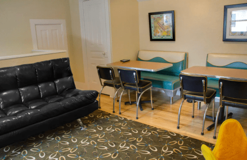 A cozy room featuring a black futon, a green and white dining set, and a patterned rug on wooden flooring.