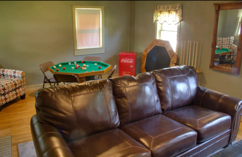 Cozy room featuring a brown couch, pool table, Coca-Cola cooler, and a mirror, with natural light from a window.