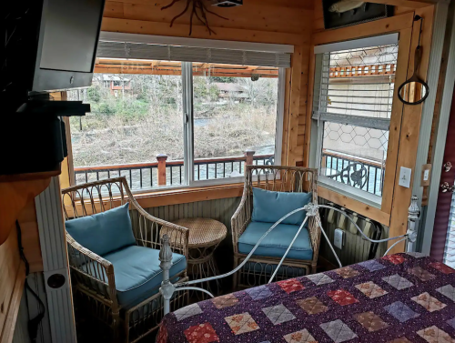 Cozy interior with two wicker chairs, a small table, and a view of a river through large windows.