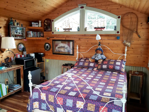 Cozy bedroom with wooden walls, a patterned quilt, a stuffed doll on the bed, and nautical decor.