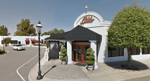 Exterior view of a restaurant with a black awning, potted plants, and a sign reading "Alibi's" on a sunny street.