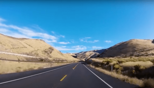 A scenic highway stretches through rolling hills under a clear blue sky.