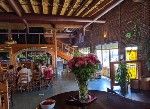 Interior of a restaurant featuring brick walls, wooden furniture, and a vase of flowers on a table.