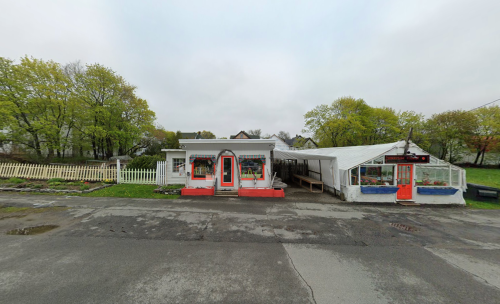 A quaint building with red doors and a greenhouse, surrounded by greenery on a cloudy day.