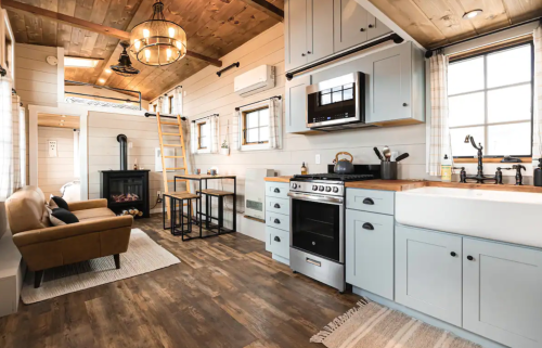 Cozy kitchen and living area with wooden accents, a sofa, dining table, and modern appliances in a bright, open space.