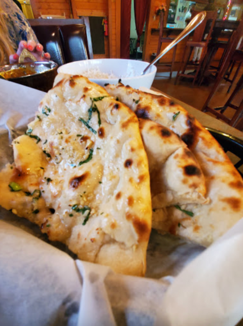 Three pieces of freshly baked naan bread with a golden-brown crust, served in a basket.