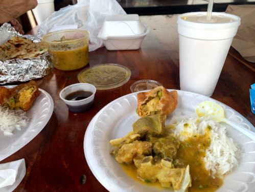 A table with plates of rice, curry, and sauces, alongside a drink in a cup and takeout containers.