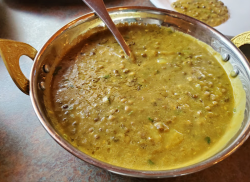 A bowl of lentil curry with a spoon, served in a traditional metal dish.