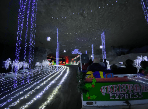 A festive tunnel decorated with colorful lights and snowflakes, viewed from a moving train.