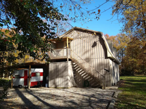 A wooden building with a staircase, surrounded by trees and a clear blue sky, in a serene outdoor setting.