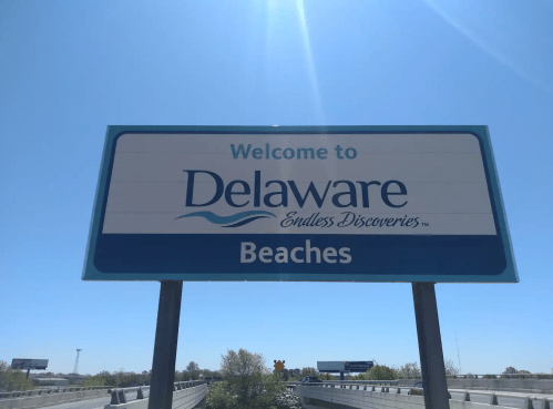 Sign welcoming visitors to Delaware, highlighting "Endless Discoveries" and "Beaches" against a clear blue sky.