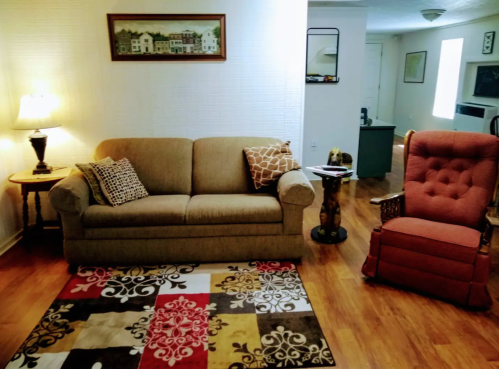 Cozy living room with a beige sofa, red armchair, patterned rug, lamp, and artwork on the walls.