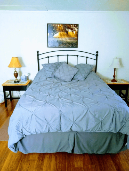 A neatly made bed with a gray comforter, two pillows, and bedside tables with lamps in a cozy room.