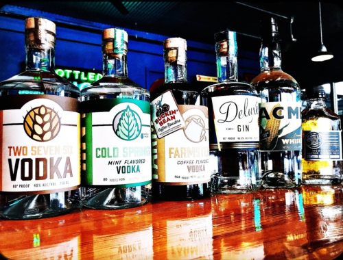 A lineup of various vodka and gin bottles on a wooden bar, featuring unique flavors and labels.