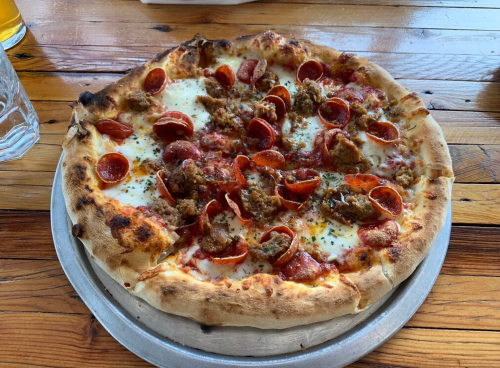 A freshly baked pizza topped with pepperoni, sausage, and melted cheese on a wooden table.