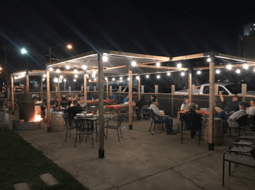 Outdoor dining area at night, with string lights and people seated around tables, creating a cozy atmosphere.