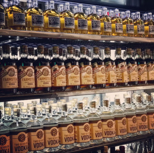 A shelf displaying various bottles of vodka, including Farmstead and Two Seven brands, arranged neatly.