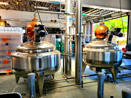 Two large, shiny stainless steel brewing kettles with copper tops in a bright, industrial brewery setting.