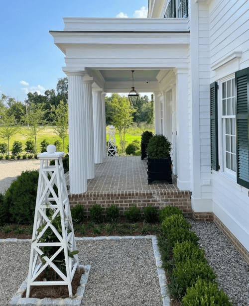 A white house with columns, a lantern, and landscaped greenery, featuring a decorative white structure in the foreground.
