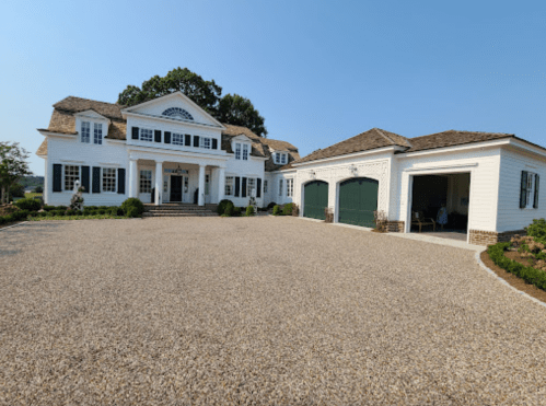 A large, white two-story house with a gravel driveway and green garage doors under a clear blue sky.