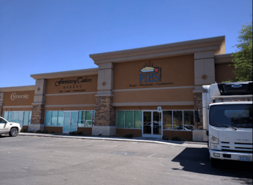 Exterior of a retail building featuring Fantasy Cakes Bakery and PIES, with a delivery truck parked nearby.