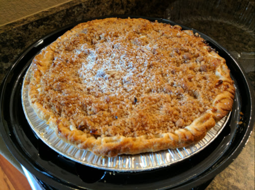 A freshly baked pie with a golden crust and crumbly topping, placed in a silver pie tin on a dark countertop.