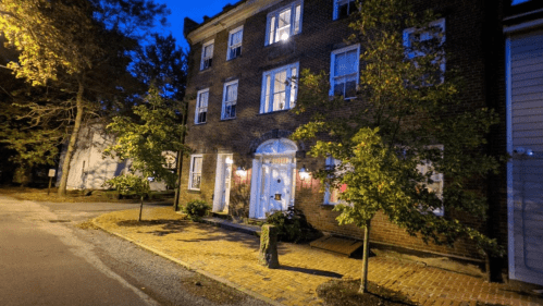 A brick building at dusk, with lit windows and trees lining the pathway, creating a cozy atmosphere.