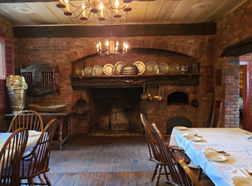 Cozy rustic kitchen with a brick fireplace, wooden chairs, and vintage cookware displayed on shelves.